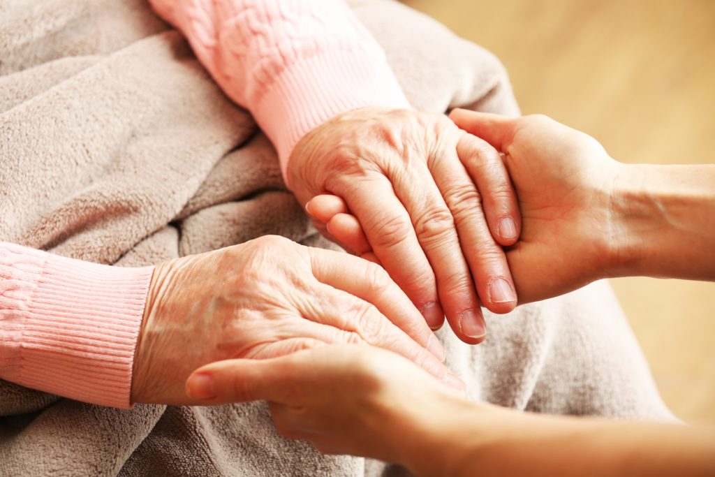 Caregiver holding an elderly woman's hands to provide comfort.