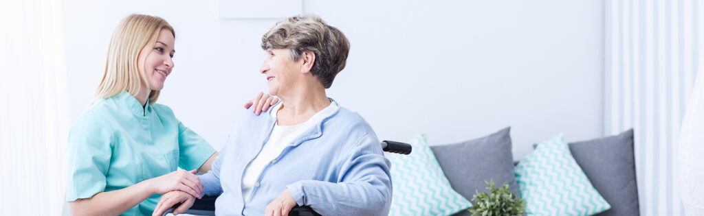 Caregiver talking with elderly women seated in a wheelchair.