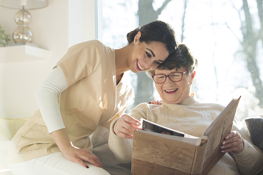 Smiling senior woman looking at a photo album with a caregiver.