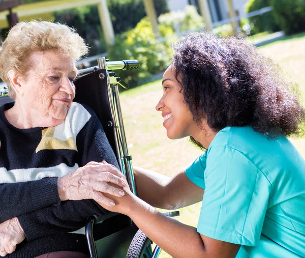 Caregiver comforting an elderly woman seated in a wheelchair outdoors.